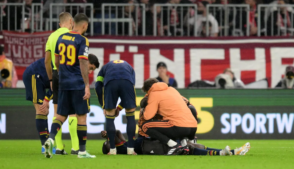 Arsenal-spelers en medische staf staan rond een geblesseerde speler op het veld tijdens een wedstrijd.