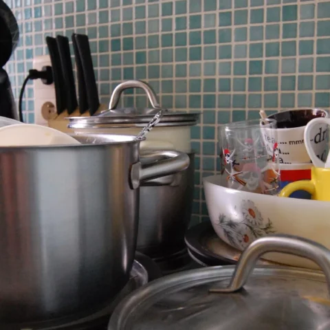 Een keuken met stapels vuile borden, pannen en mokken bij de gootsteen.