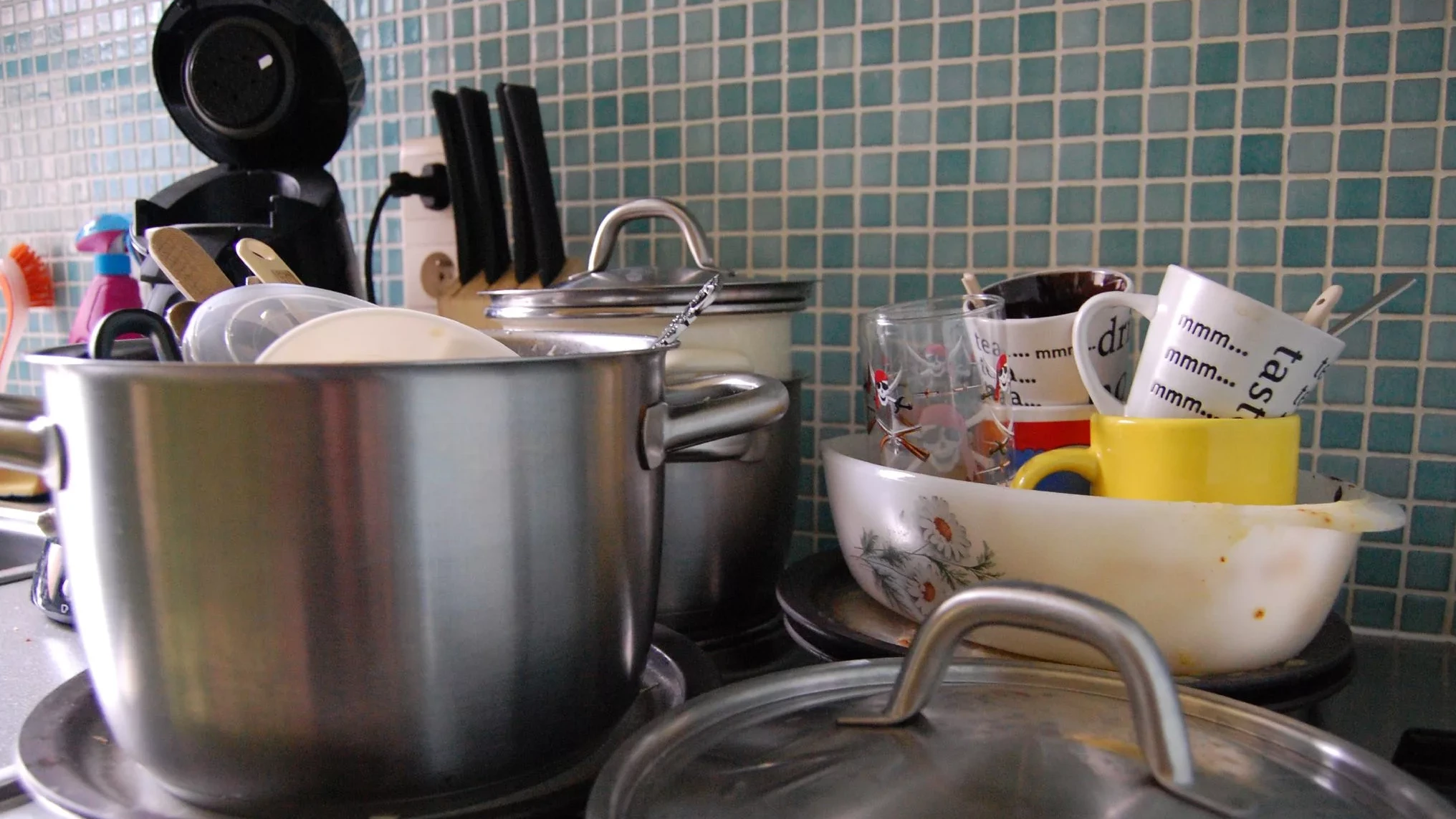 Een keuken met stapels vuile borden, pannen en mokken bij de gootsteen.