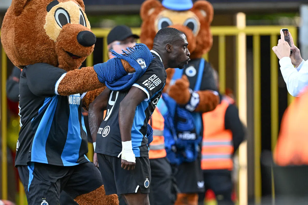 Een Club Brugge-speler loopt met een mascotte op de achtergrond bij het stadion.