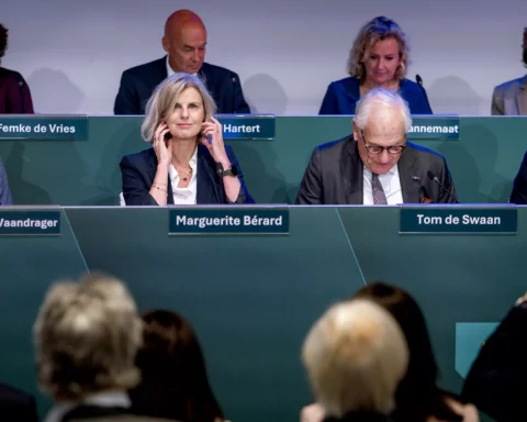 Bestuurspaneel met mannen en vrouwen achter naamplaten tijdens een bijeenkomst.
