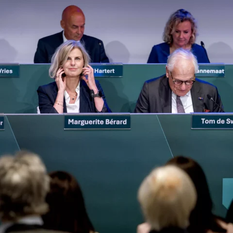 Bestuurspaneel met mannen en vrouwen achter naamplaten tijdens een bijeenkomst.