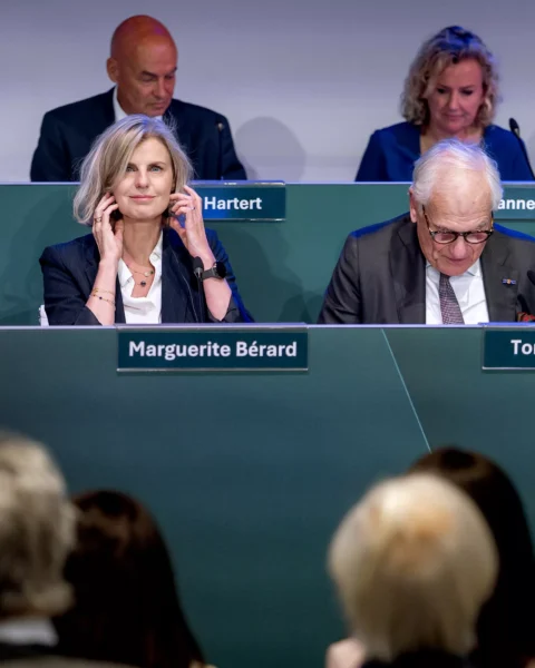 Bestuurspaneel met mannen en vrouwen achter naamplaten tijdens een bijeenkomst.