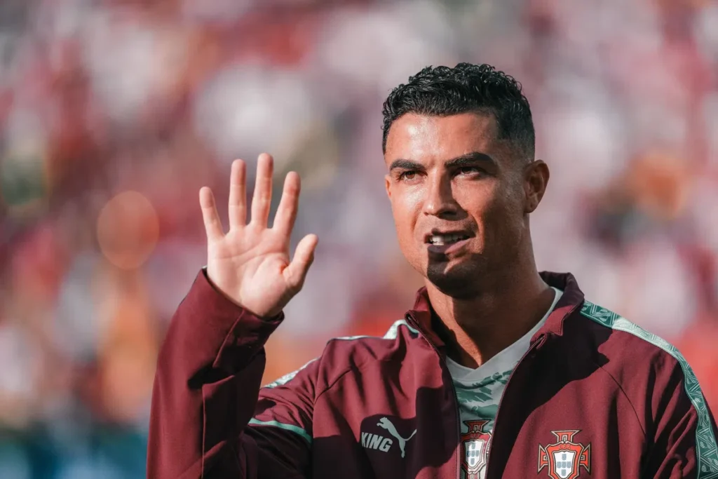 Cristiano Ronaldo zwaait tijdens een voetbalwedstrijd in een Portugese trainingsjas.