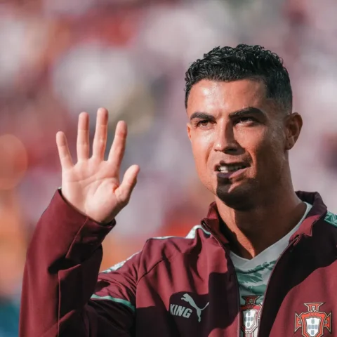 Cristiano Ronaldo zwaait tijdens een voetbalwedstrijd in een Portugese trainingsjas.