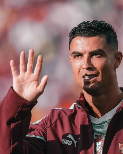 Cristiano Ronaldo zwaait tijdens een voetbalwedstrijd in een Portugese trainingsjas.