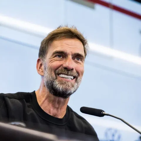 Jürgen Klopp smiles tijdens een persmoment achter een microfoon.