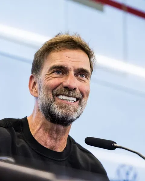 Jürgen Klopp smiles tijdens een persmoment achter een microfoon.