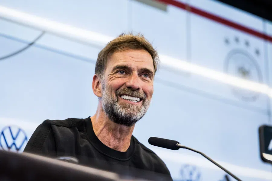 Jürgen Klopp smiles tijdens een persmoment achter een microfoon.