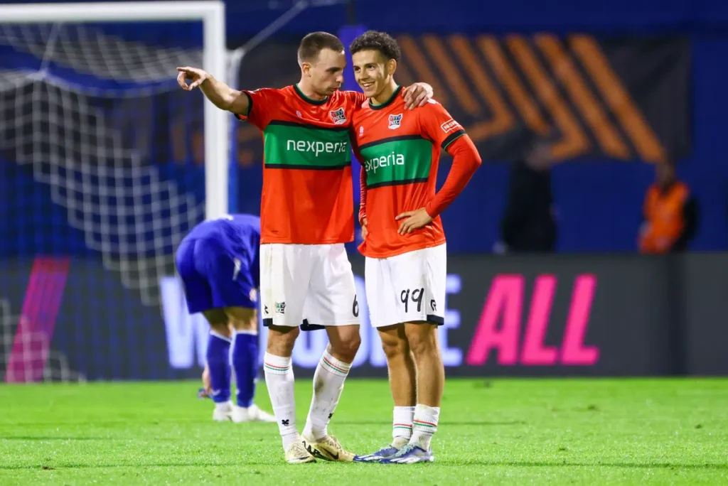 Twee NEC-spelers staan samen op het veld tijdens de wedstrijd.