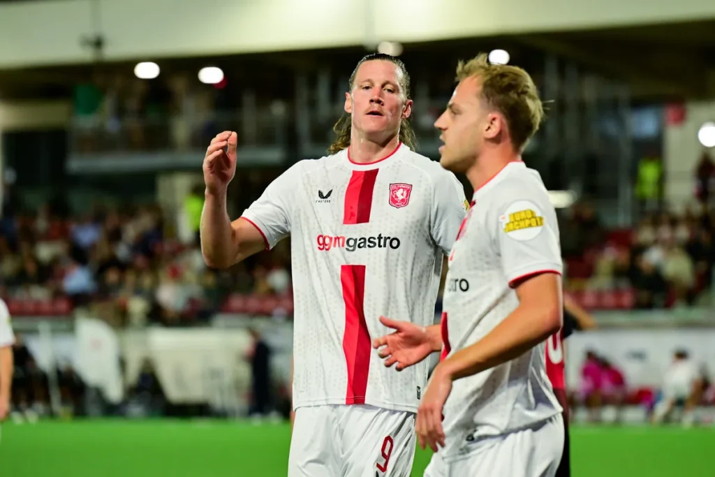 Twee FC Twente-spelers in witte uitshirts op het veld tijdens een wedstrijd.