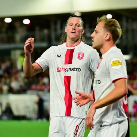 Twee FC Twente-spelers in witte uitshirts op het veld tijdens een wedstrijd.