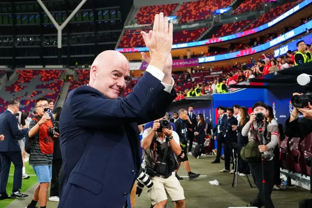 Gianni Infantino klapt in een stadion terwijl fotografen hem omringen.