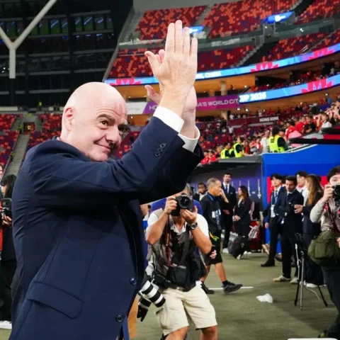 Gianni Infantino klapt in een stadion terwijl fotografen hem omringen.