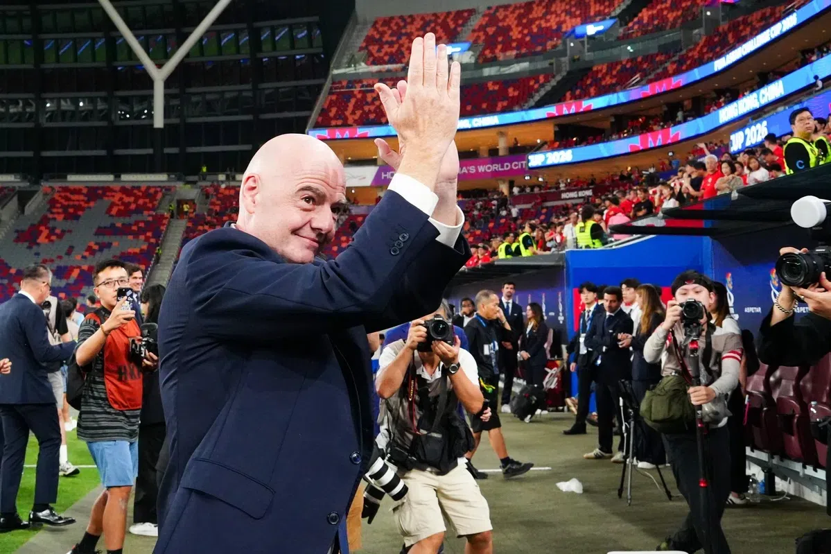Gianni Infantino klapt in een stadion terwijl fotografen hem omringen.