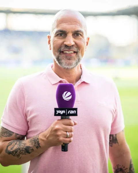 Markus Babbel houdt een microfoon vast in een stadion tijdens een interview.