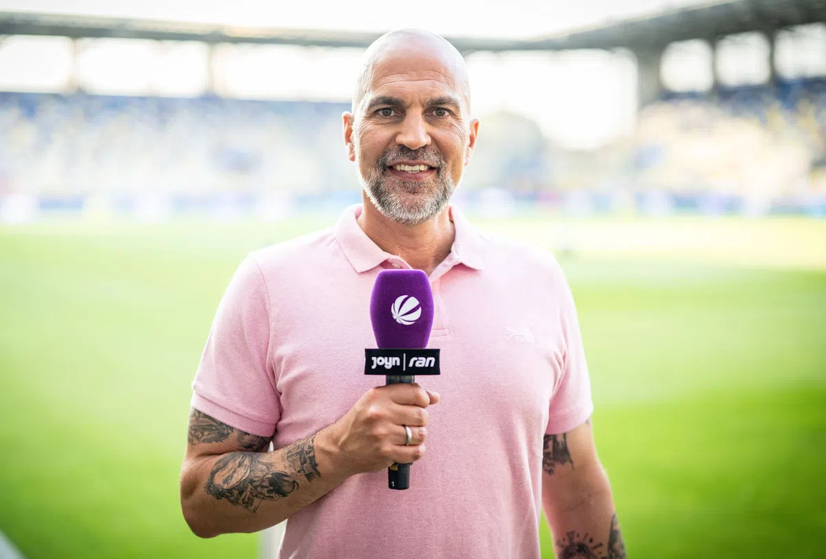 Markus Babbel houdt een microfoon vast in een stadion tijdens een interview.