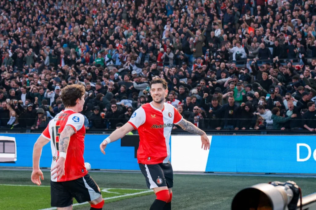 Twee Feyenoord-spelers vieren een moment op het veld voor een volle tribune.