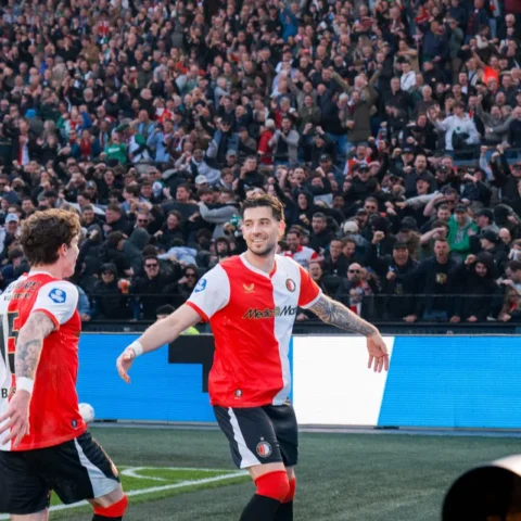 Twee Feyenoord-spelers vieren een moment op het veld voor een volle tribune.
