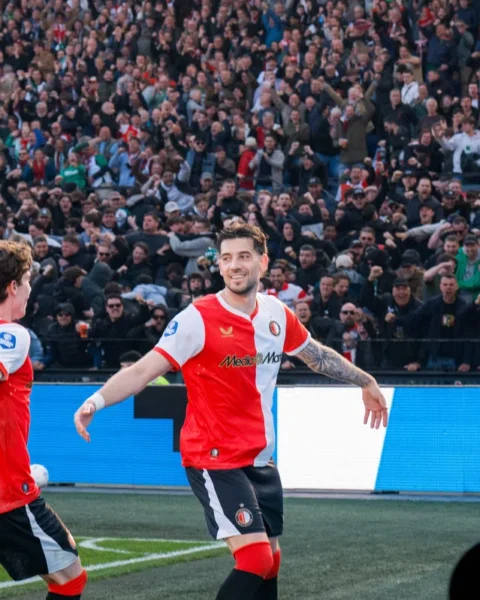 Twee Feyenoord-spelers vieren een moment op het veld voor een volle tribune.