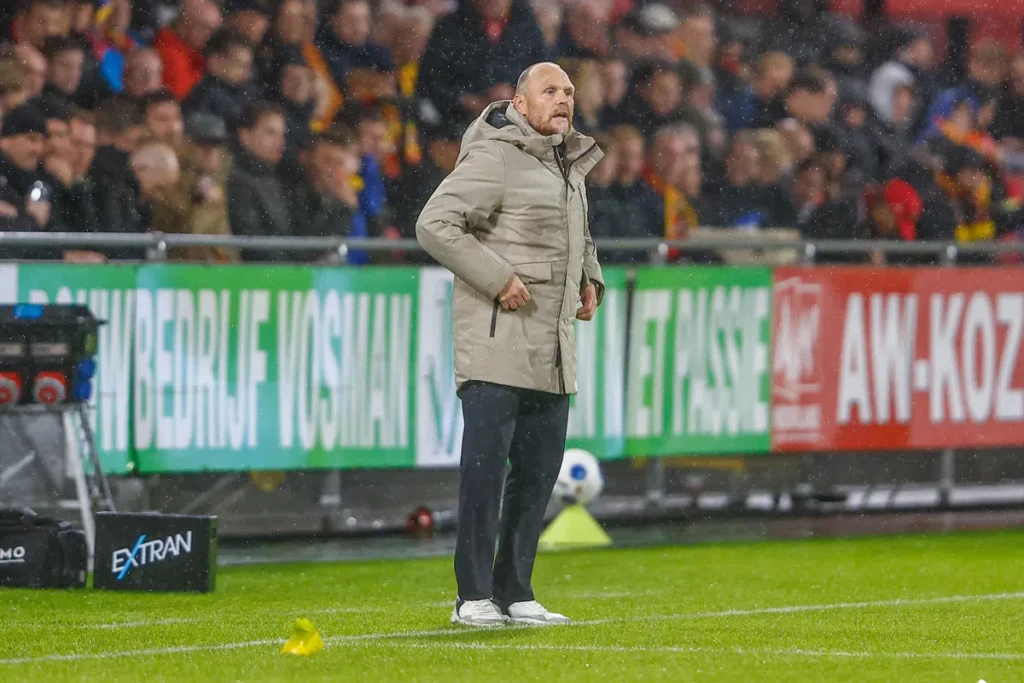 Joseph Oosting staat langs de zijlijn tijdens een voetbalwedstrijd in de regen.