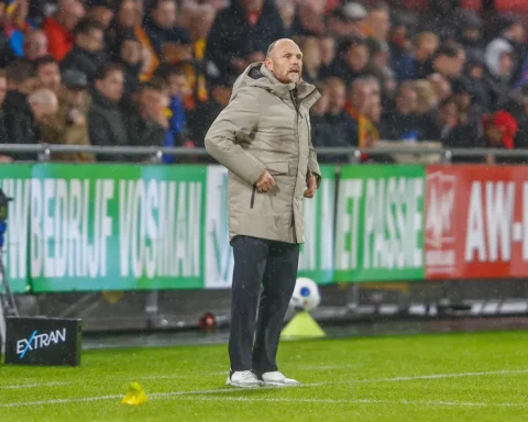 Joseph Oosting staat langs de zijlijn tijdens een voetbalwedstrijd in de regen.