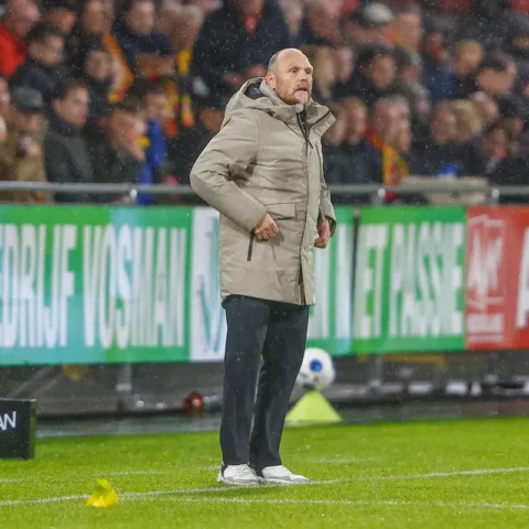Joseph Oosting staat langs de zijlijn tijdens een voetbalwedstrijd in de regen.