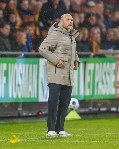 Joseph Oosting staat langs de zijlijn tijdens een voetbalwedstrijd in de regen.