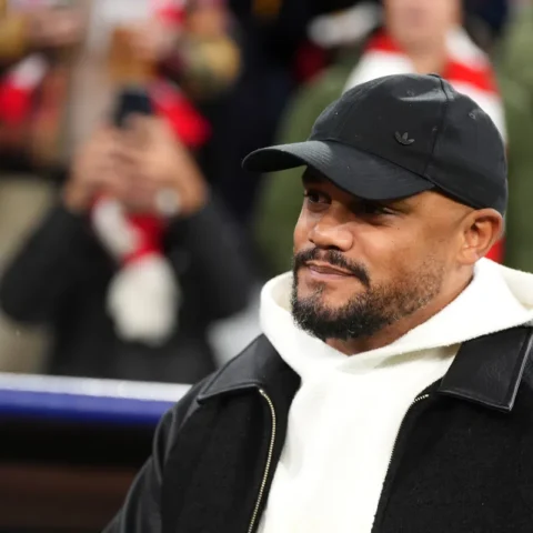 Vincent Kompany draagt een zwarte pet en witte hoodie bij een voetbalwedstrijd.