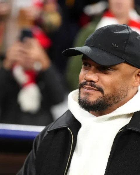 Vincent Kompany draagt een zwarte pet en witte hoodie bij een voetbalwedstrijd.