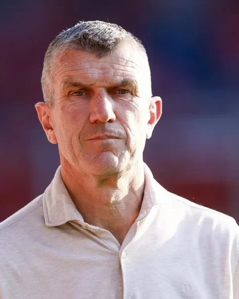 Portret van een man in een licht polohemd op een stadionachtergrond.
