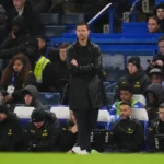Xabi Alonso staat met gekruiste armen langs de zijlijn tijdens een voetbalwedstrijd, met Chelsea-spelers en staf op de bank achter hem.
