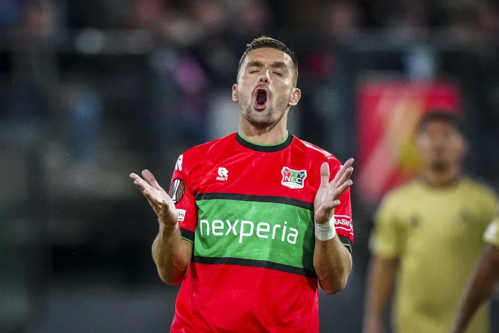 Dusan Tadic van NEC in rood-groen shirt tijdens een wedstrijd, met open mond en geheven handen.