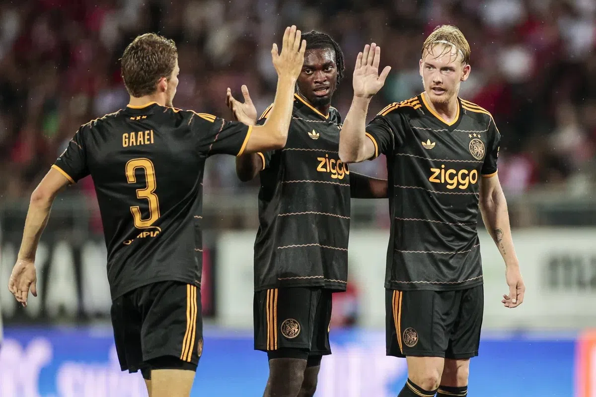Drie Ajax-spelers in zwarte uitshirts geven elkaar een high-five op het veld.