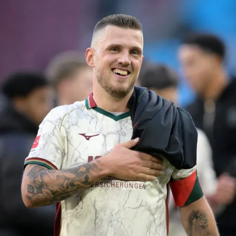 Jeffrey Gouweleeuw lacht op het veld in een FC Augsburg-shirt.