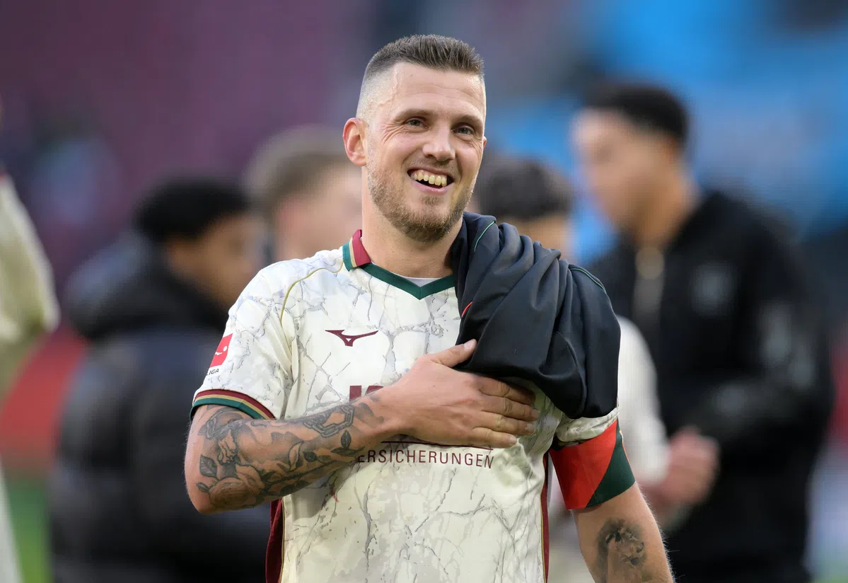 Jeffrey Gouweleeuw lacht op het veld in een FC Augsburg-shirt.