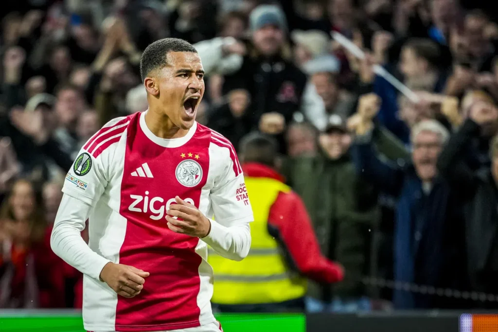 Ajax-speler in rood-wit tenue juicht op het veld.