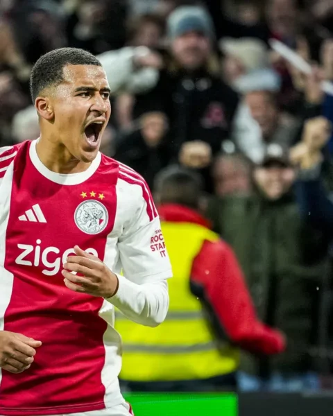 Ajax-speler in rood-wit tenue juicht op het veld.
