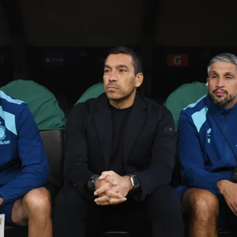 Giovanni van Bronckhorst zit op de bank naast Feyenoord-stafleden tijdens een wedstrijd.