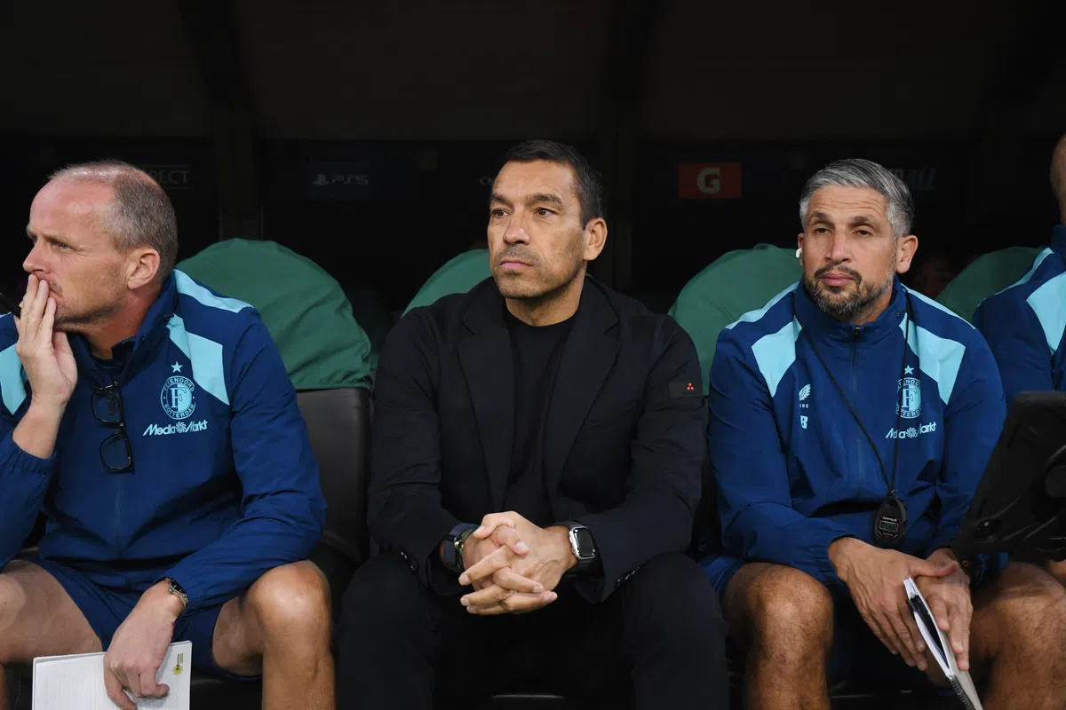 Giovanni van Bronckhorst zit op de bank naast Feyenoord-stafleden tijdens een wedstrijd.