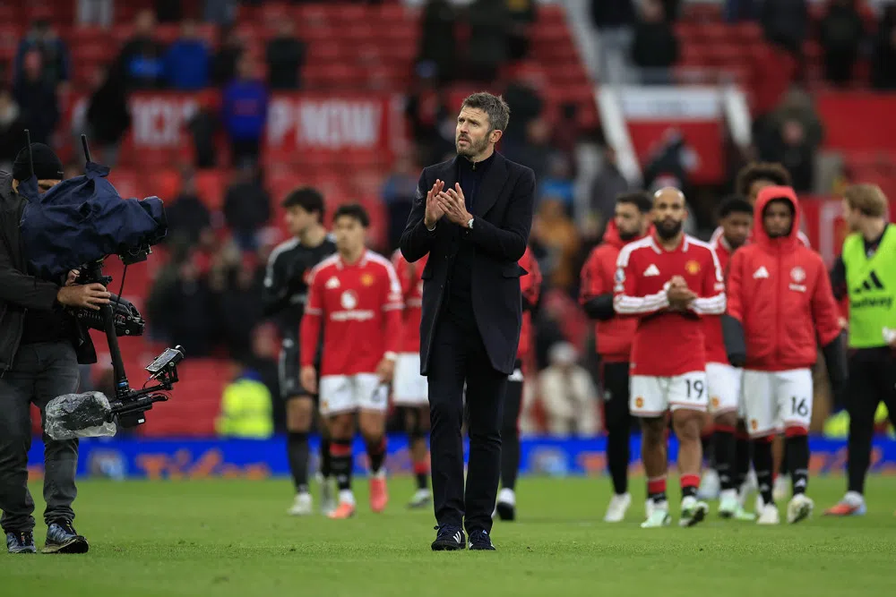 Michael Carrick staat op het veld te applaudisseren, met Manchester United-spelers op de achtergrond.