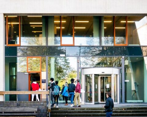Mensen staan bij de ingang van een modern overheidsgebouw met draaideur en glazen gevel.