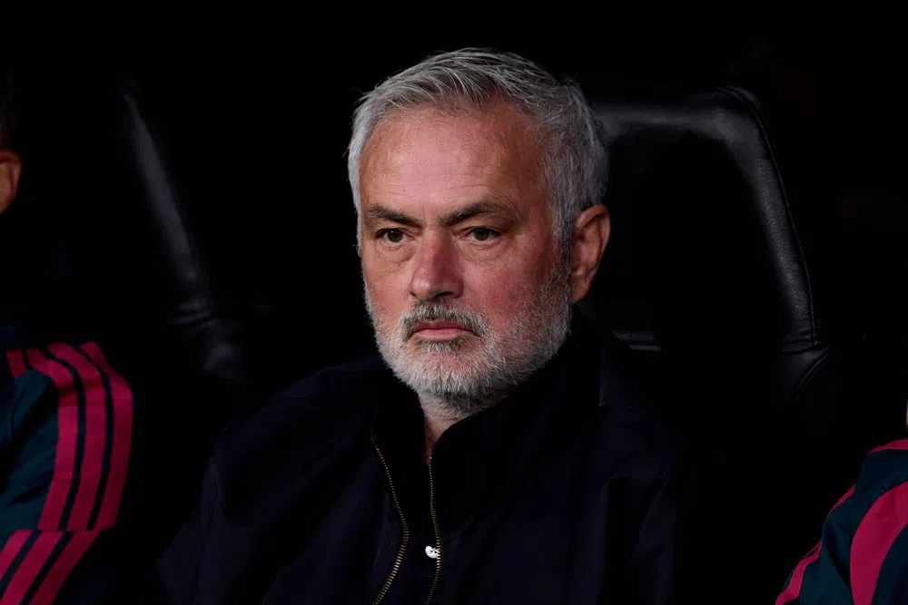 José Mourinho zit op de bank en kijkt ernstig voor zich uit.