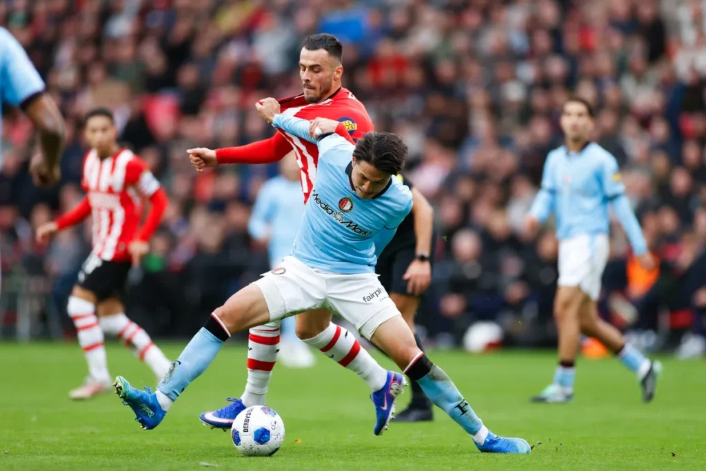 Voetballers van Feyenoord en PSV in duel om de bal op het veld.