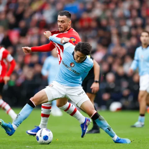 Voetballers van Feyenoord en PSV in duel om de bal op het veld.
