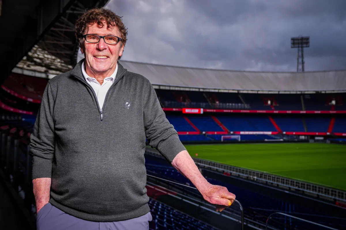 Willem van Hanegem staat in een voetbalstadion met het veld en de tribunes op de achtergrond.