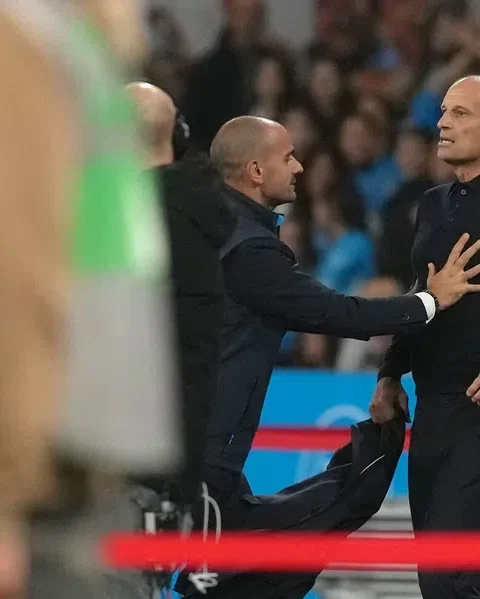 Massimiliano Allegri staat langs de zijlijn tijdens een voetbalwedstrijd terwijl een official hem aanspreekt.