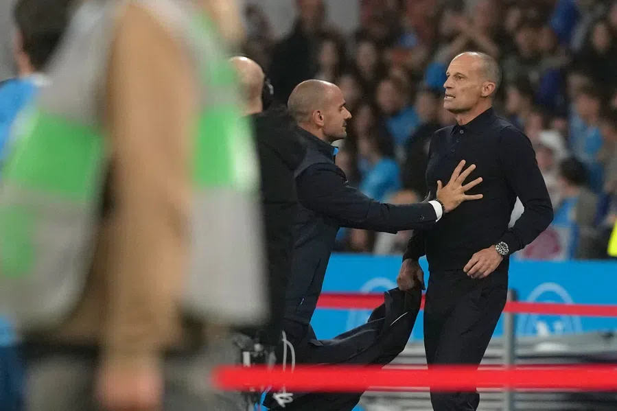Massimiliano Allegri staat langs de zijlijn tijdens een voetbalwedstrijd terwijl een official hem aanspreekt.