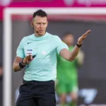 Scheidsrechter in lichtblauw shirt geeft een armgebaar langs het veld.