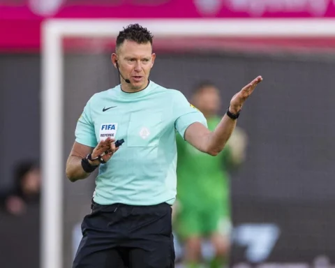 Scheidsrechter in lichtblauw shirt geeft een armgebaar langs het veld.